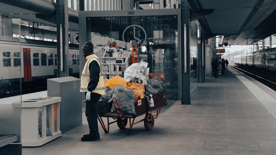 A photograph of a clean, organized outdoor area showing a pile of various discarded waste materials, including cardboard boxes, plastic containers, and mixed household items stacked on a paved drivewa